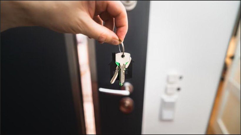Hand holding house keys in front of an open front door